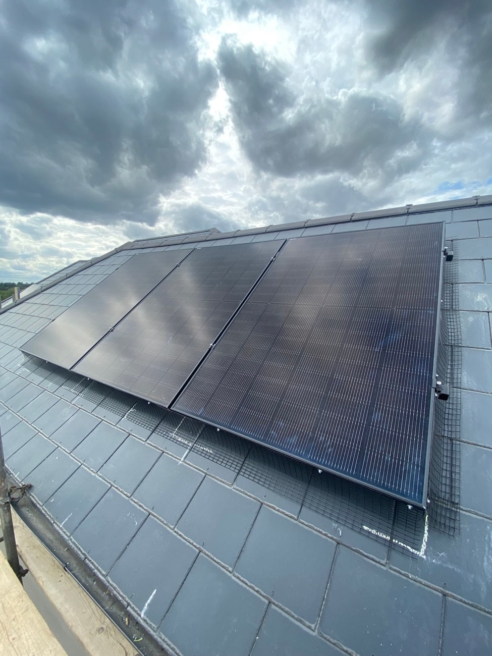 Black solar panels on a slate roof beneath dramatic clouds