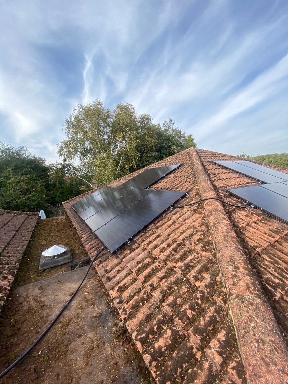 Black solar panels installed on a tiled roof under a blue sky