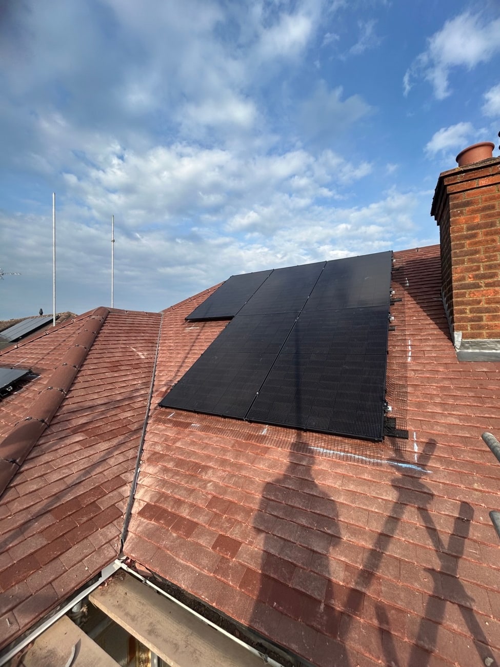Black solar panels on a red tiled roof with a chimney