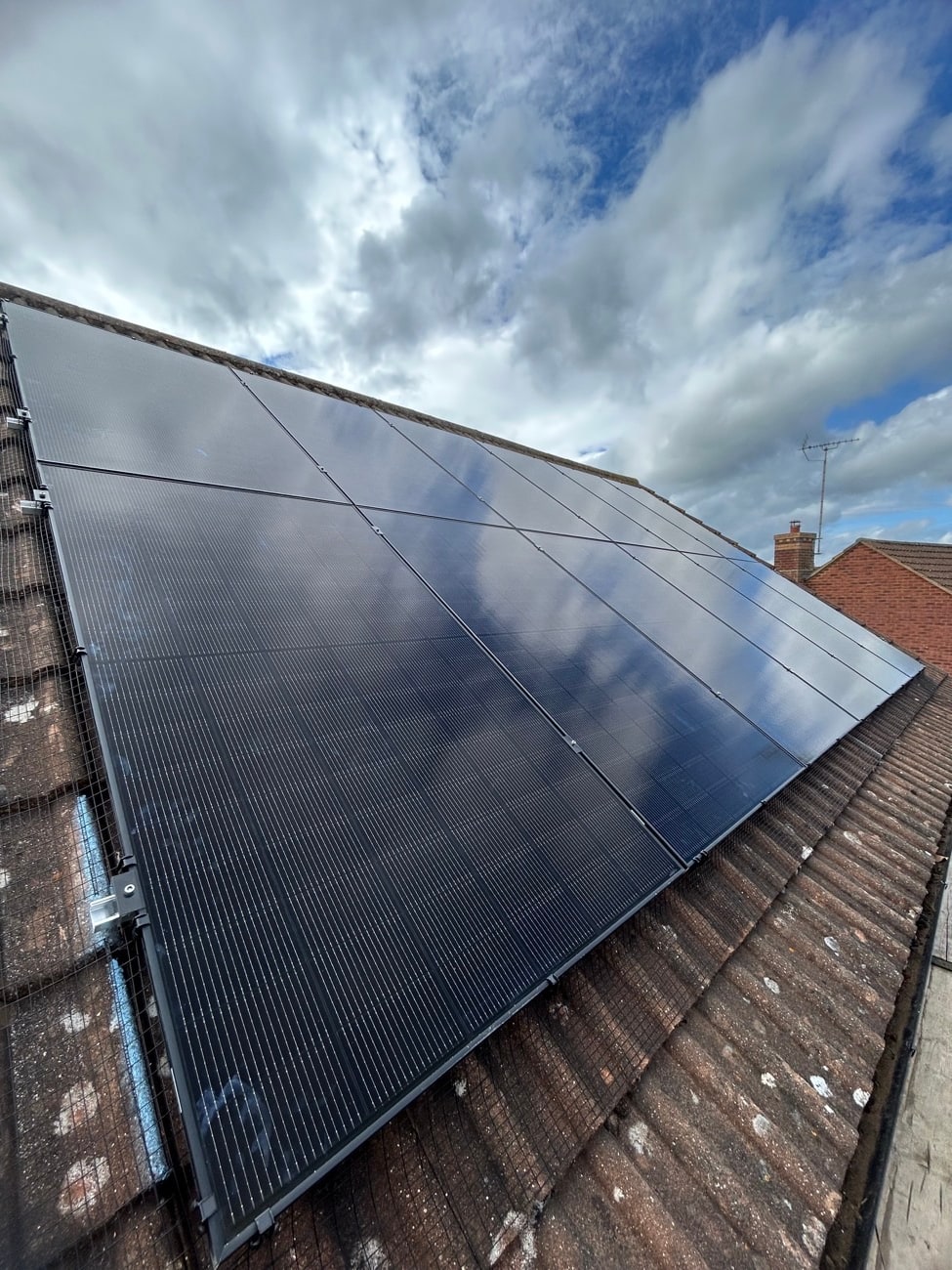 All-black solar panel array on a tiled roof against a dramatic sky