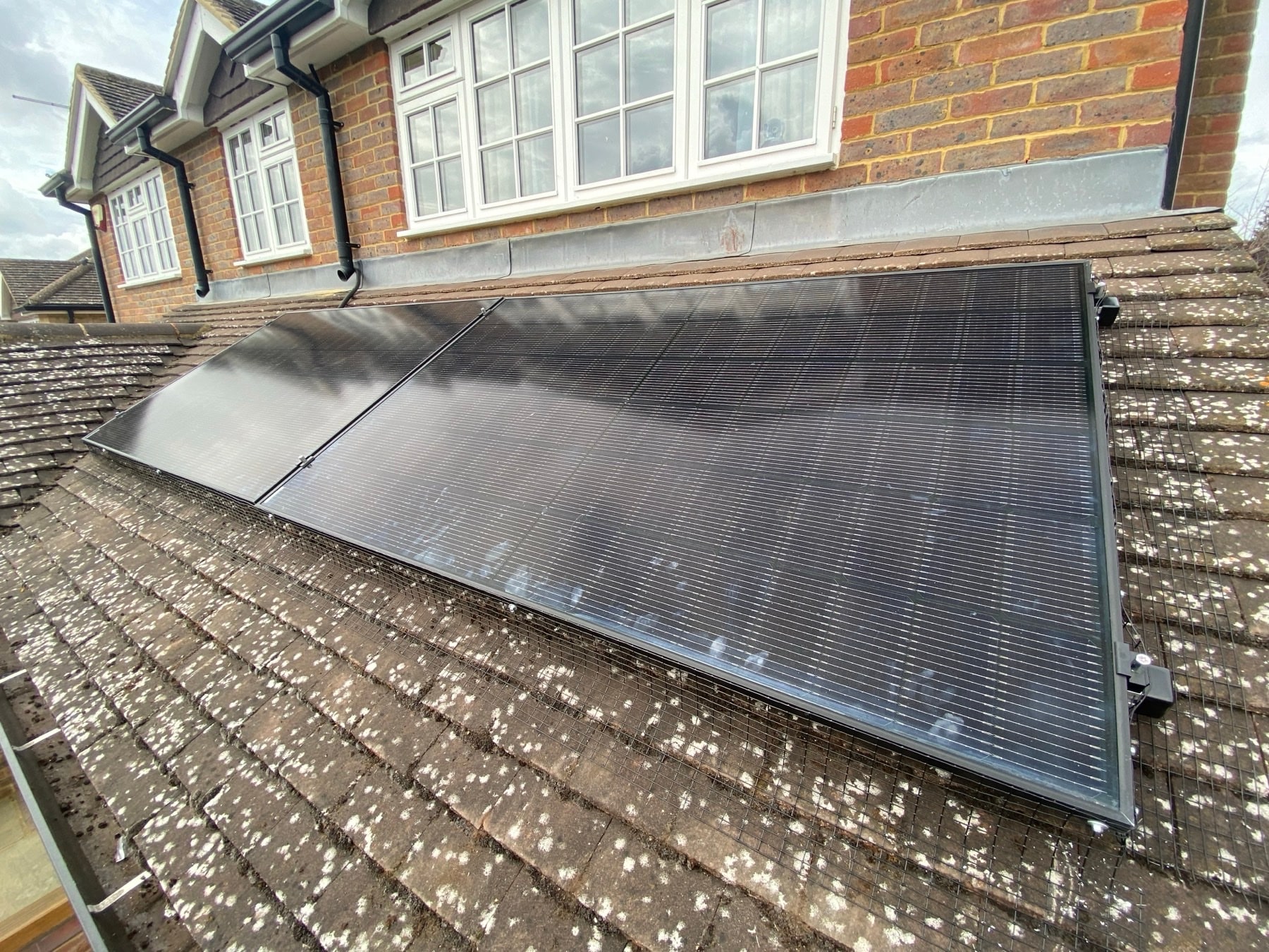 Black solar panels on a tiled roof beside a brick house