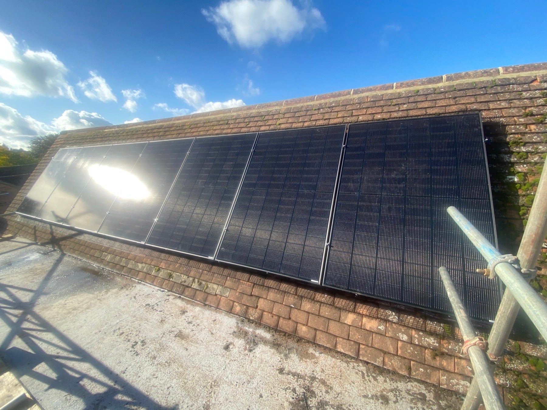 Black solar panels on a brick house roof against a blue sky