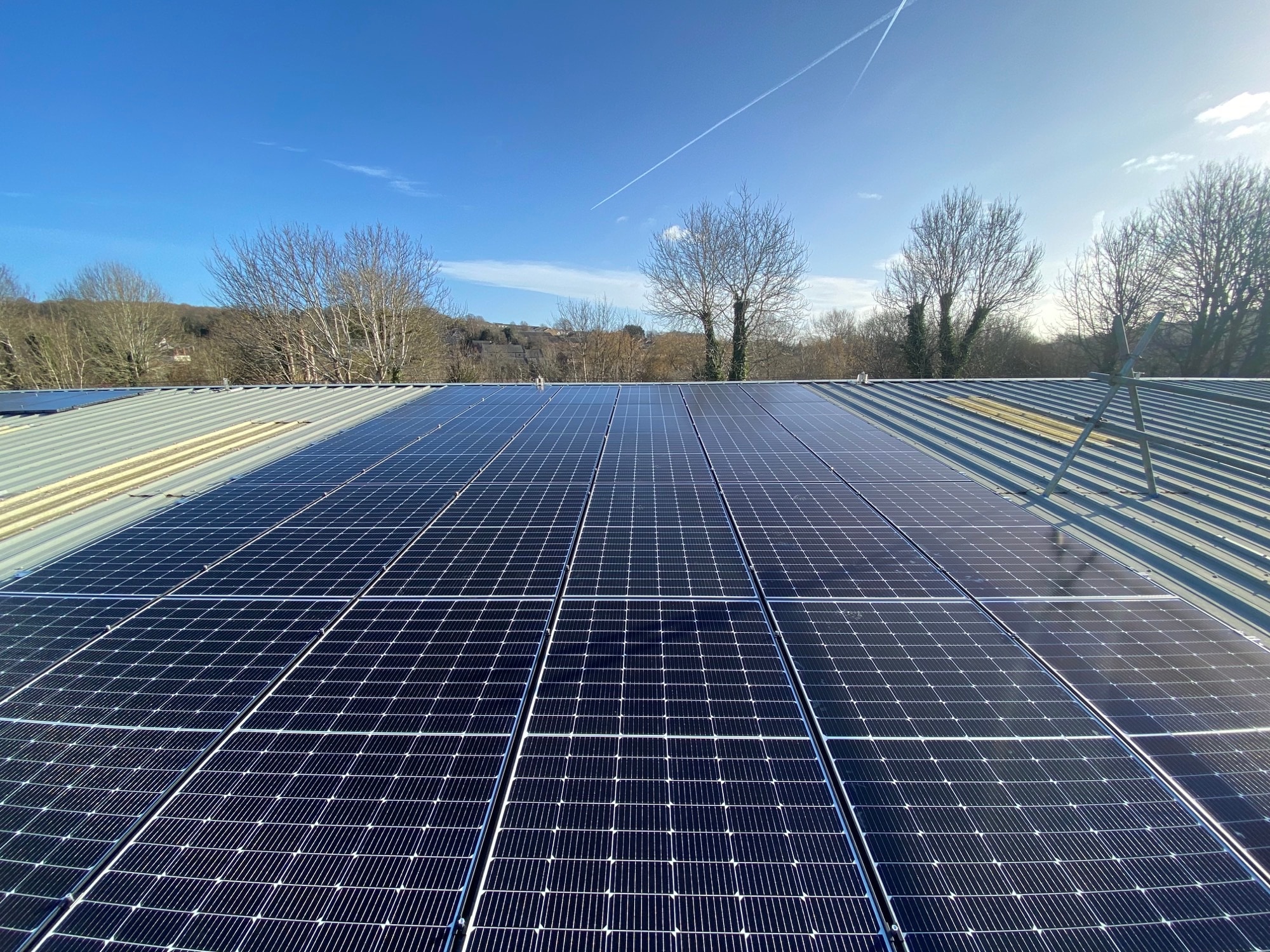 Black solar panels professionally installed across a large roof against a clear blue sky in Hertfordshire